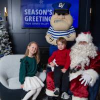 Boy and girl smile sitting on Santa's lap with Louie standing